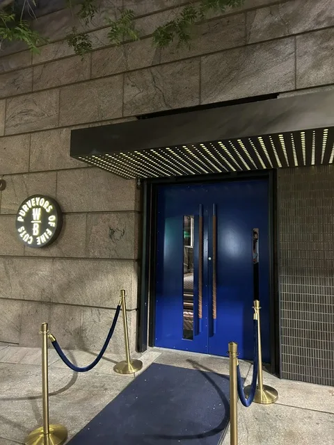 Wicked Butcher entrance at night — blue doors, gold stanchions, and the WB Purveyors of Fine Cuts sign